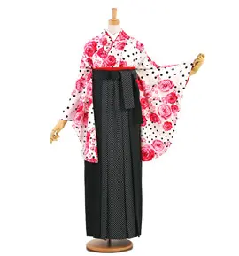 ピンク、赤、白の花柄と水玉模様の着物を着たマネキン。白い水玉模様の黒い紋付のスカートと、白い水玉模様の黒い紋付のスカートがセットされています。マネキンは無地の背景に立っています。.