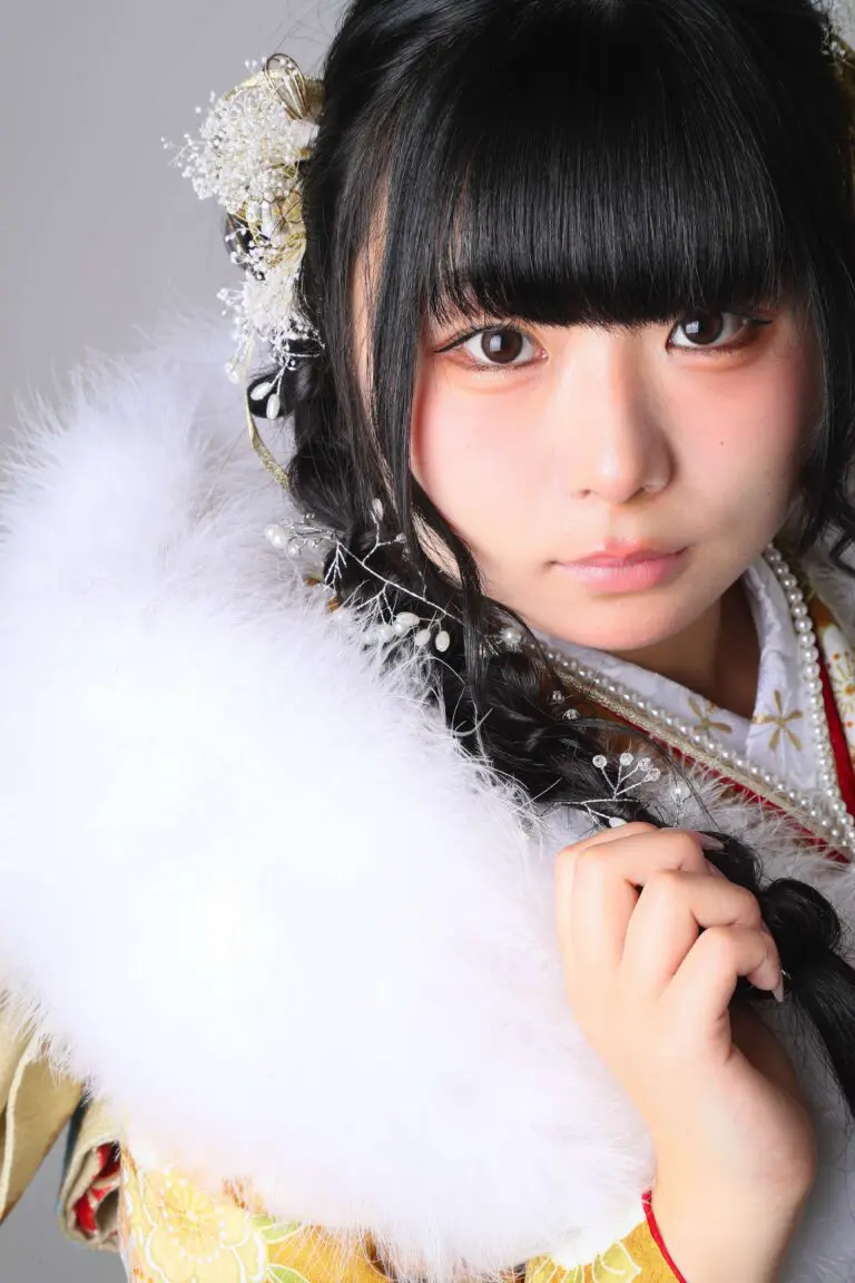 華やかな髪飾りとふわふわの白いスカーフを身につけた日本の伝統的な着物を着た若い女性。前髪のあるストレートの黒髪で、ニュートラルな背景を背景にカメラをまっすぐ見つめている。.