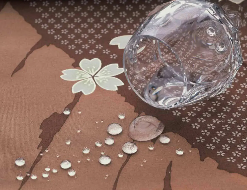 透明なガラスのコップが、花柄の茶色の布の上に横たわって置かれ、こぼれた水滴が表面に玉のように溜まっています。.