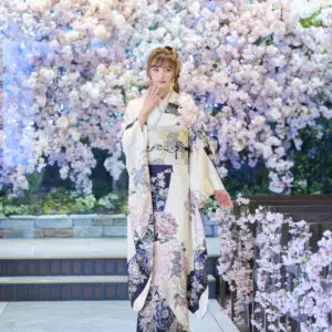 M-402柄の着物を着た人物が、屋内の磨き上げられた床の上に立っている。背景には満開の桜の木があり、階段の横に立っている。.