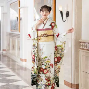 大理石の床とウォールアートが施された廊下に、K-120-色とりどりの花柄が描かれた白い着物に金の帯を締めた人物が立っている。髪には飾りをつけ、着物の袖を広げている。.